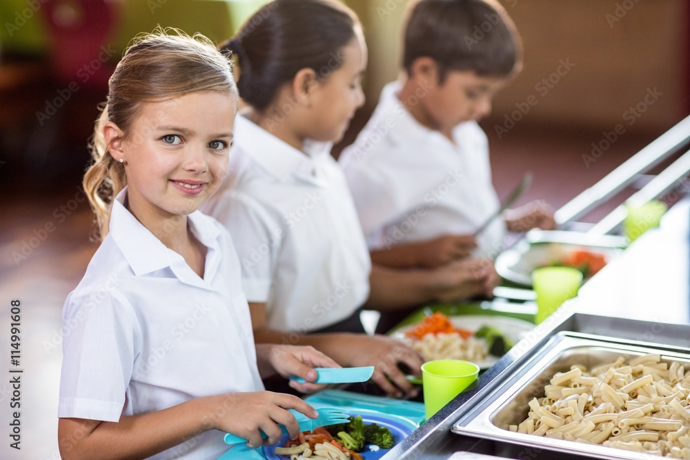 Fototapeta premium Schoolgirl with classmate standing near canteen counter
