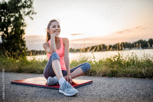 Smiling Fitness Girl Sitting After Exercise by the Riverside