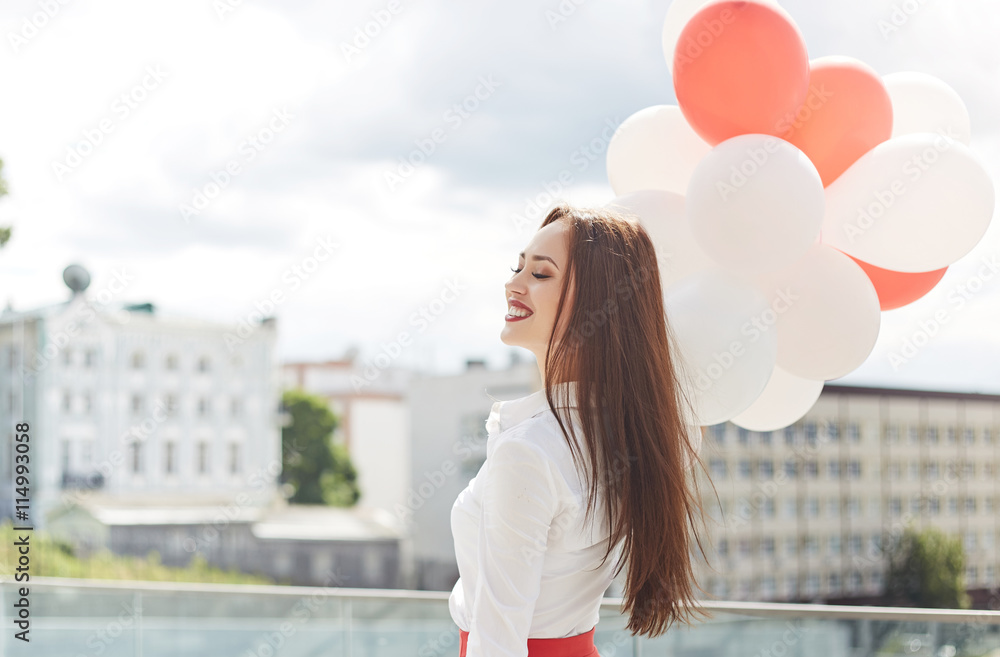 Beautiful young woman with balloons with closed eyes on the background of the city. Summer concept. 