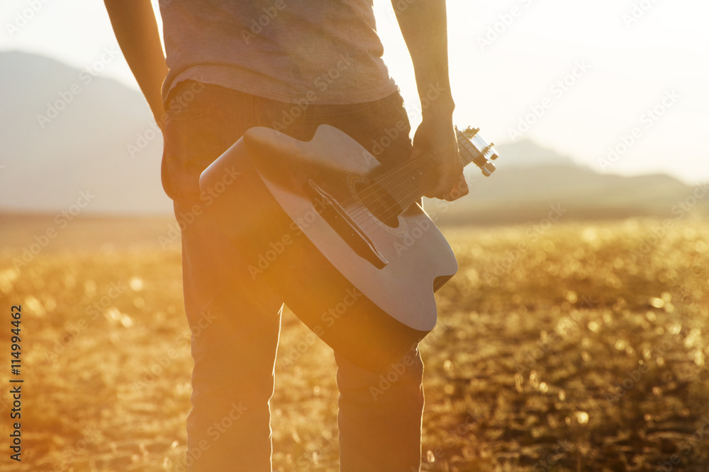 Obraz premium Closeup photo of man with guitar on sunset backdrop