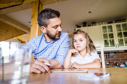 Father and daughter sitting at home using digital tablet