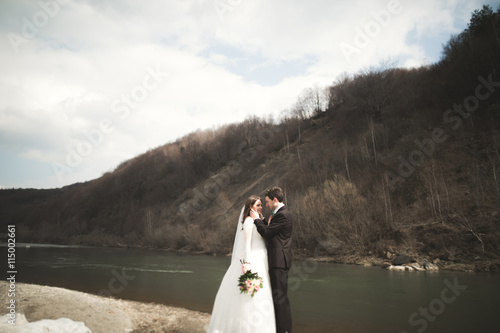 Happy wedding couple  bride and groom posing neat river against backdrop of the mountains