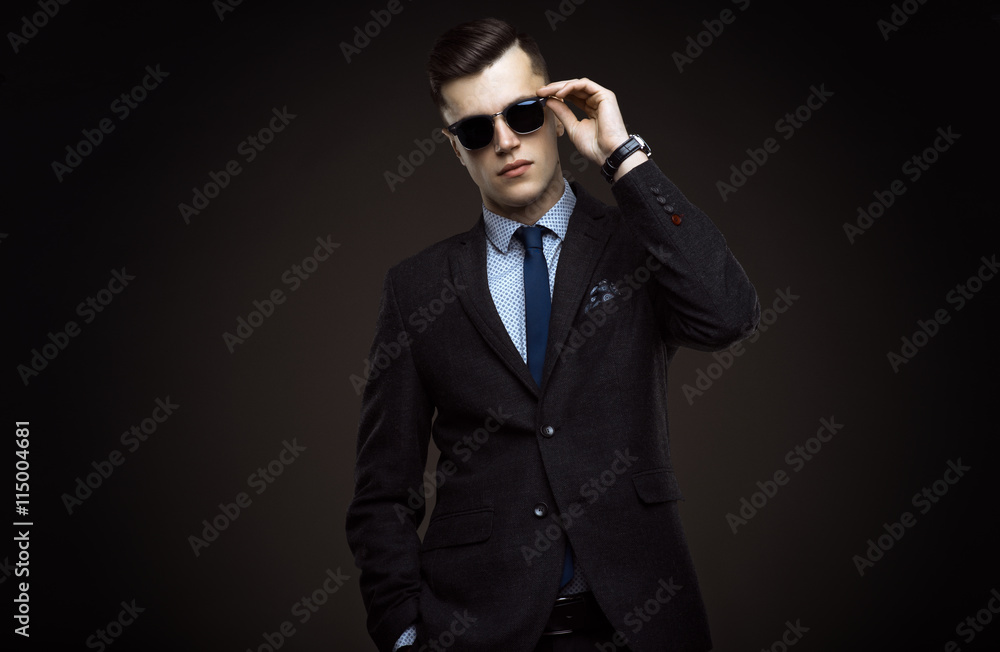Stylish young man in suit and sunglasses. Business style. Fashionable image. Office worker. Sexy man standing and looking at the camera Stylish young man in suit and sunglasses. Business style. Fashionable image. Office worker. Sexy man standing and looking at the camera