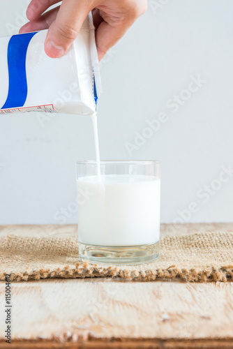 Hand holding a carton of milk poured into a glass on white backg
