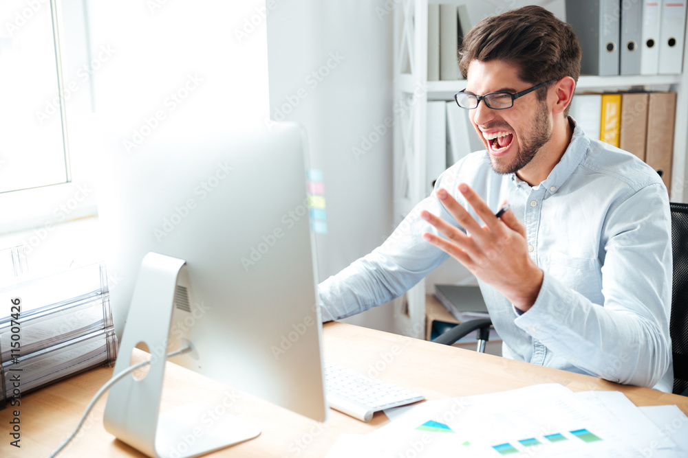 Angry mad young businessman working with computer and shouting