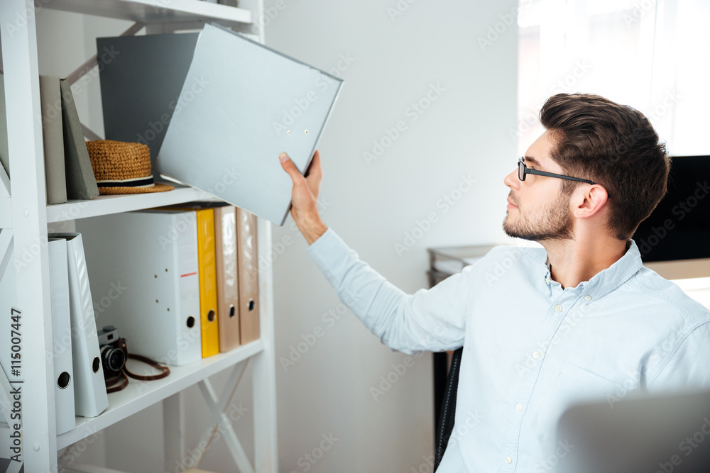 Attractive businessman sitting and taking folder with documents in office