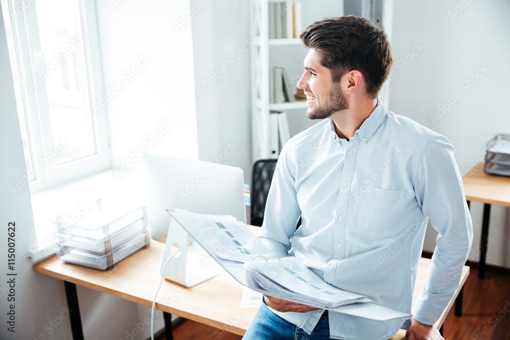 Happy young businessman holding folder with documents in office