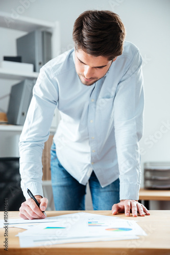 Serious young businessman writing on the table in office