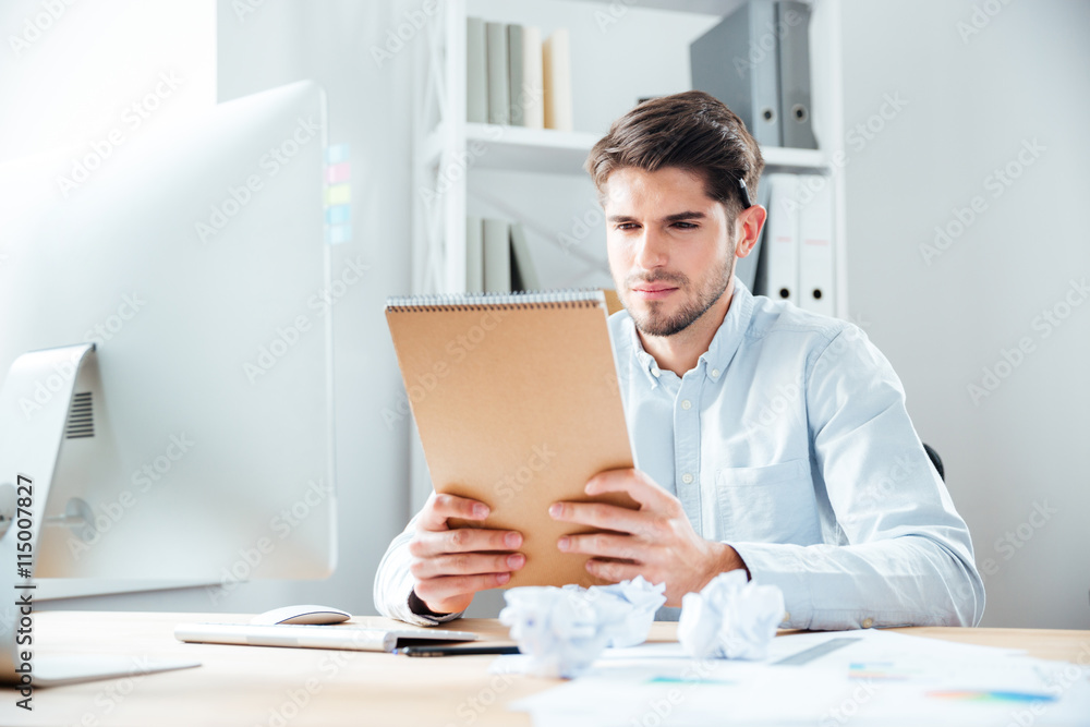 Handsome young businessman man sitting and reading notes in notebook Handsome young businessman man sitting and reading notes in notebook