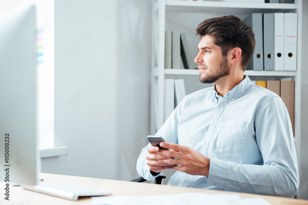 Businessman sitting at his workplace in office with mobile phone Businessman sitting at his workplace in office with mobile phone