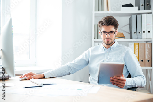 Young businessman sitting and using tablet computer in office