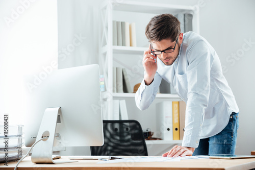 Business man standing at desk working on documents with mobilephone