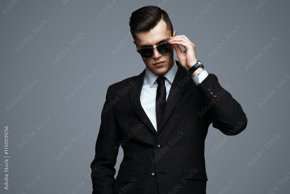 Stylish young man in suit and sunglasses. Business style. Fashionable image. Office worker. Sexy man standing and looking at the camera Stylish young man in suit and sunglasses. Business style. Fashionable image. Office worker. Sexy man standing and looking at the camera