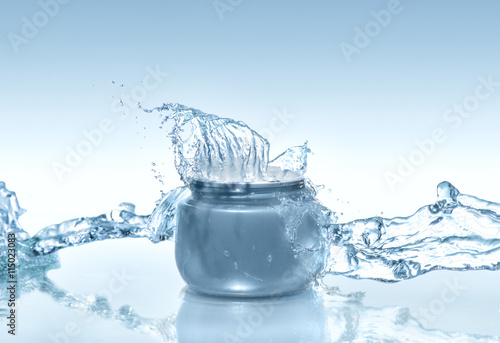 The blue jar of moisturizing cream with big water splash and water stream around on the gradient blue background