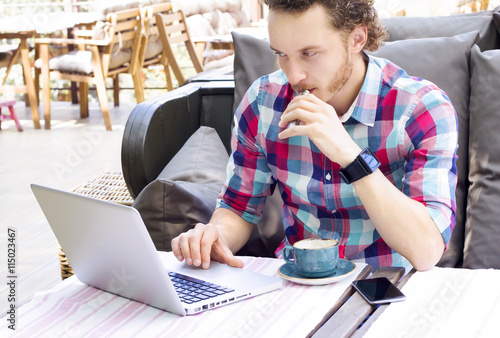 Style man with laptop sitting in a cafe  outdoor and smoking electronic cigarette. Handsome man working in cafe.