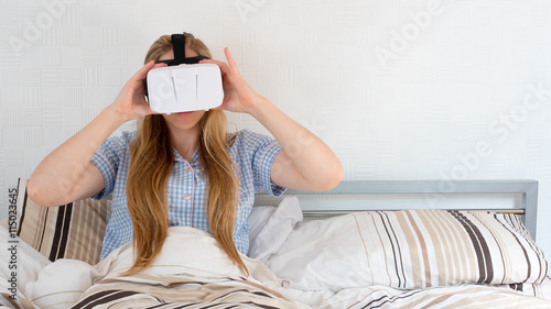 Beautiful woman using VR headset in bed with controller photo