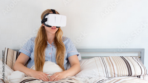 Beautiful woman using VR headset in bed with controller photo