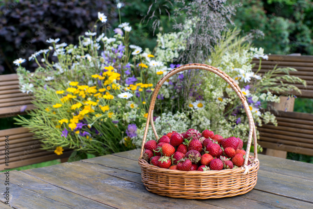 Strawberries in a wicker basket on a background of summer bouque