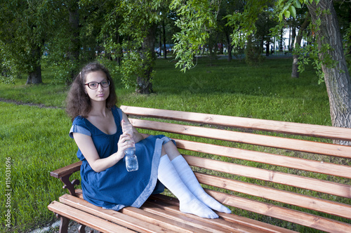 The girl opens a bottle of water on a bench