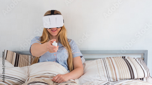 Beautiful woman using VR headset in bed with controller photo