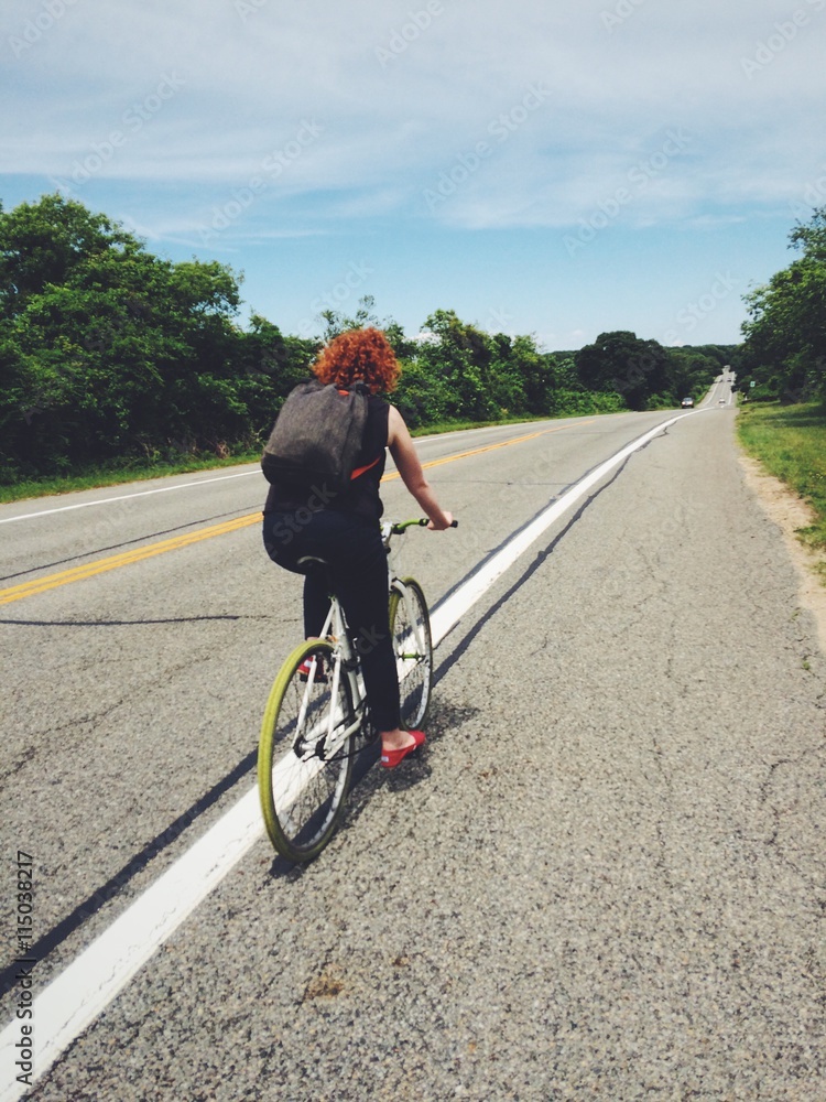 Fototapeta premium Red head woman riding bike along highway