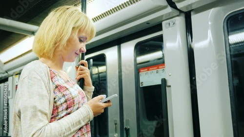 A young woman reading a message on the phone, going to the subway. Standing near the door the wagon