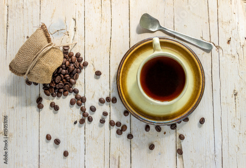 Чашка черного кофе и кофейные зерна на деревянном фоне.