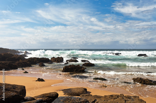 The coast of the Atlantic Ocean. Volcanic stones on yellow sand. Beautiful seascape. Portugal, Algarve