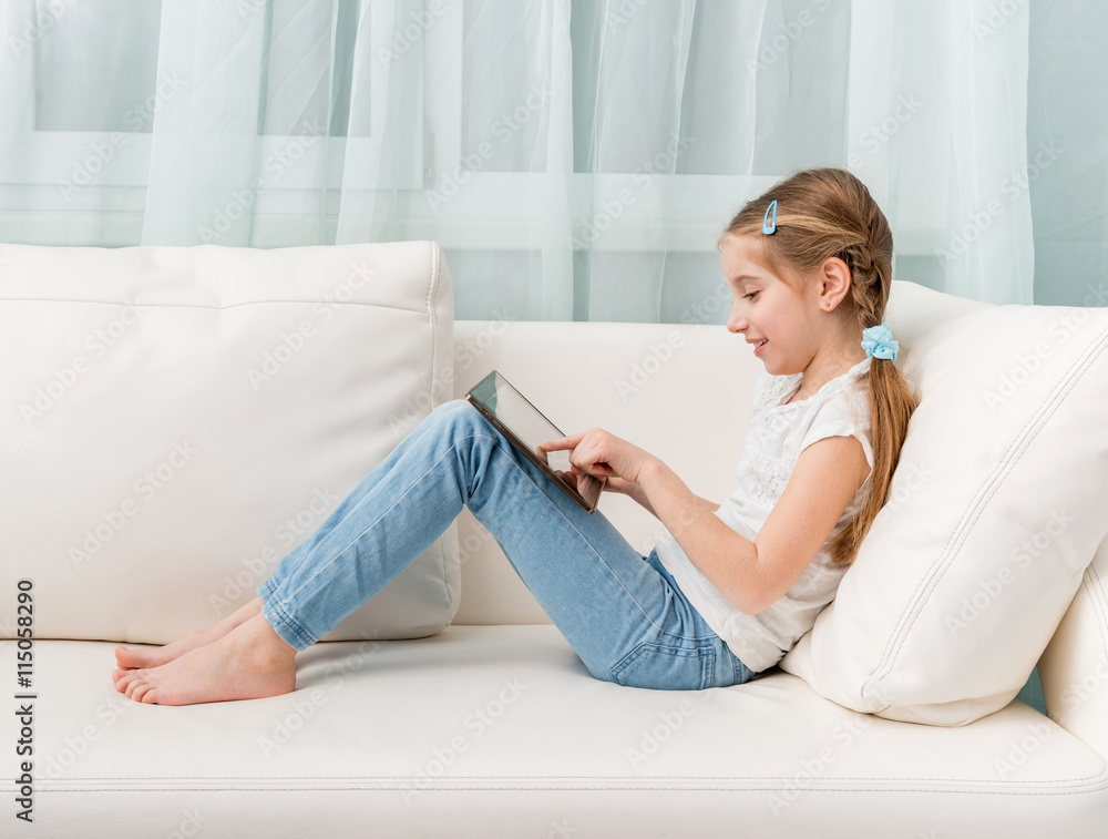 little girl sitting on white sofa looks at tablet touching it, profile  photo foto de Stock | Adobe Stock