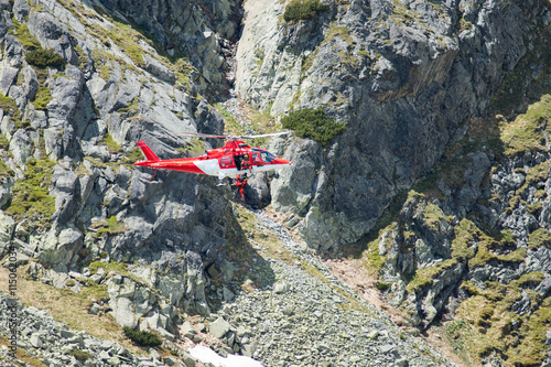 red and white emergency rescue helicopter in high mountains saving and transporting injured hiker