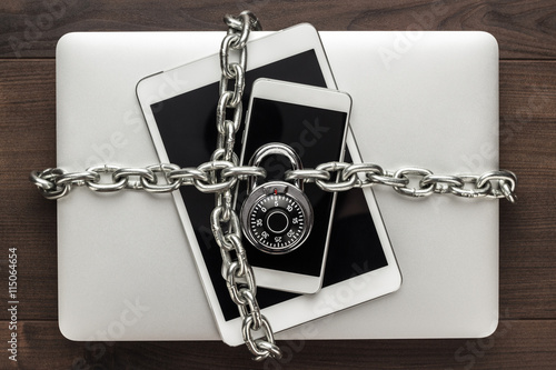 data security concept: computer, tablet, phone bound by metal chain and closed with combination lock on wooden table photo