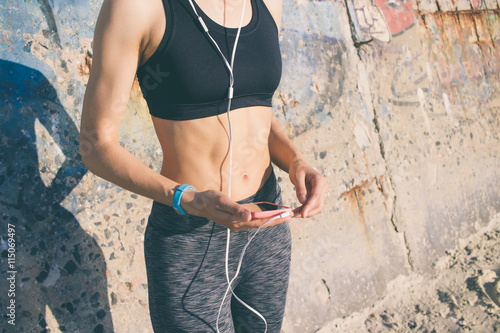 Athletic girl in sportswear is listening to music with headphone