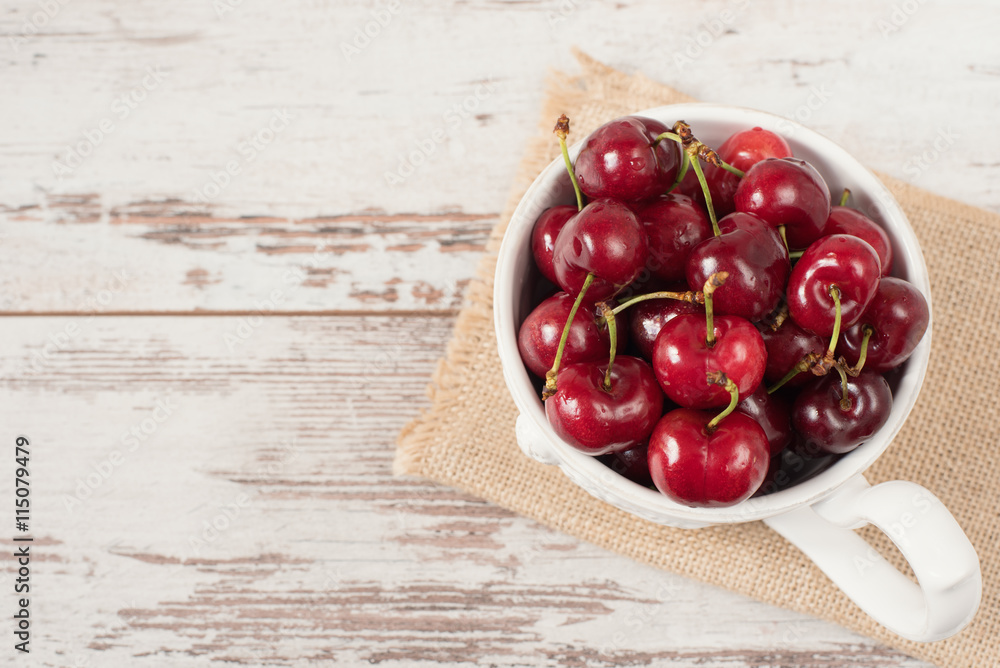 A large cup of coffee in front angel, white bowl full with fresh cherries, fruits. Light rustic background, shabby chic, vintage tinting, top view, copy space in left A large cup of coffee in front angel, white bowl full with fresh cherries, fruits. Light rustic background, shabby chic, vintage tinting, top view, copy space in left