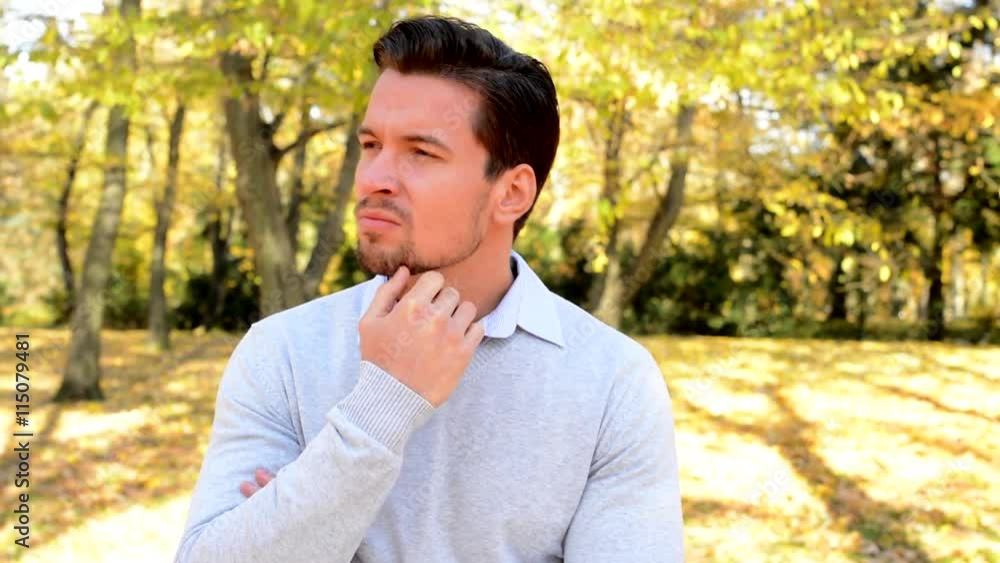 Young handsome man stands in the woods, strokes his chin, looks worried and thinks about something Young handsome man stands in the woods, strokes his chin, looks worried and thinks about something