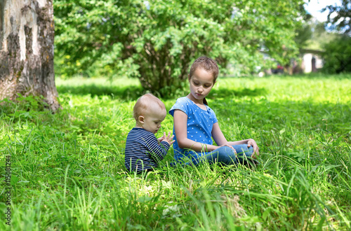 baby boy and little girl sitting playing on grass in park © AlexandraBudzinskaya