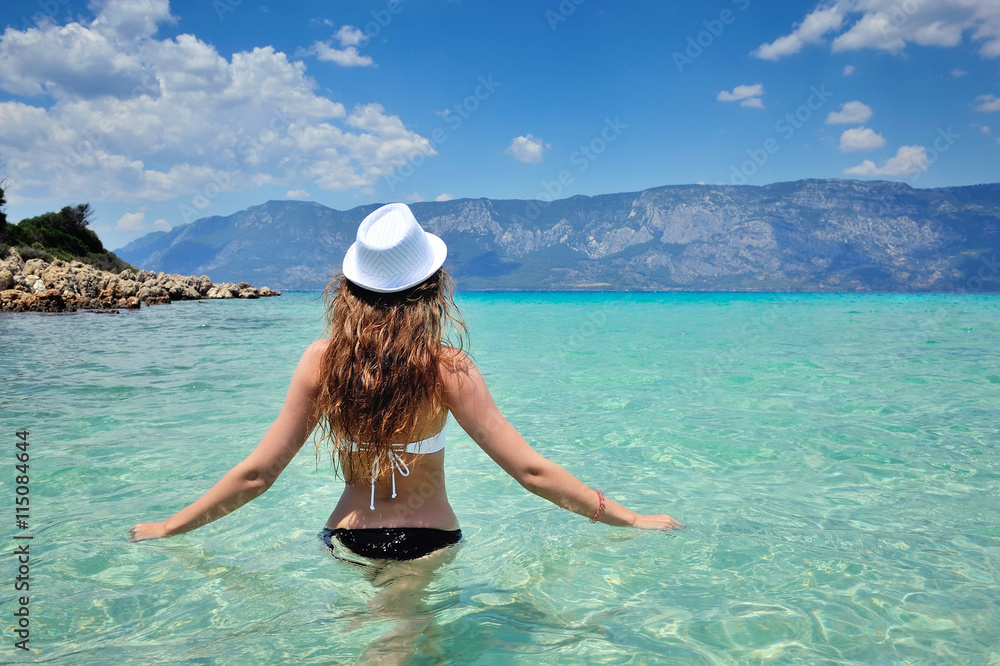 Rear view of young beautiful girl hat and bikini in the sea transparent water