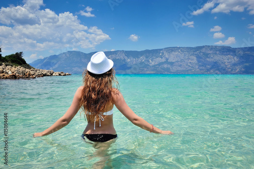 Rear view of young beautiful girl hat and bikini in the sea transparent water