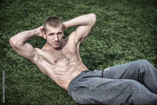 Outdoor training. Young man doing exercises for abdominal muscles on green grass. © Yarkovoy