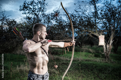 Archery. A young man aiming a bow at a target photo