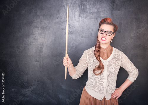 Angry teacher with pointer on blackboard background photo