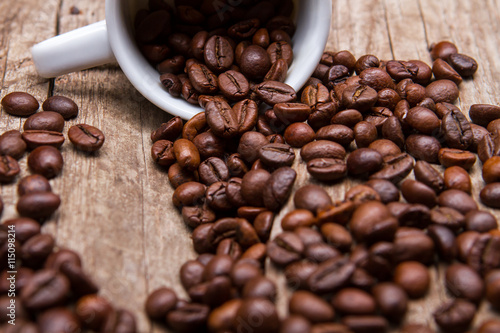 Cup with roasted coffee beans. Coffee grains of dark color. Fresh aroma of arabica. Cup on old brown shelf.