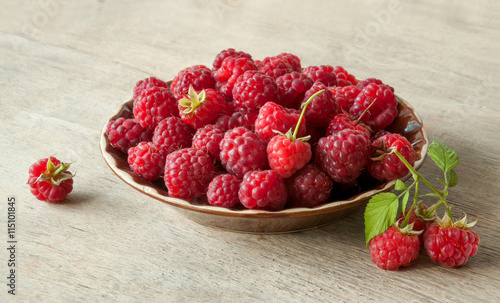 Ripe sweet raspberries in bowl on wooden table