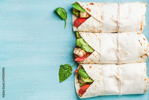 Healthy lunch snack. Three tortilla wraps with grilled chicken fillet and fresh vegetables over turquoise blue painted wooden background. Top view, copy space