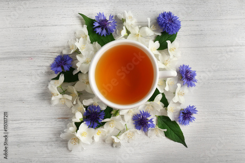 Cup of tea with fresh flowers lying around on wooden background