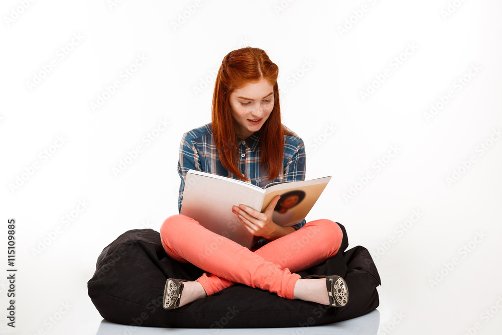 Obraz premium Portrait of beautiful ginger girl reading magazine over white background.