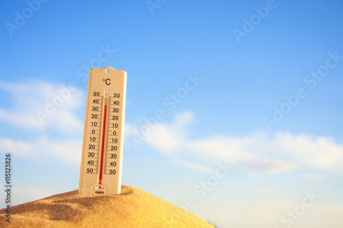 Thermometer with celsius scale on warm beach sand showing extreme high temperature.