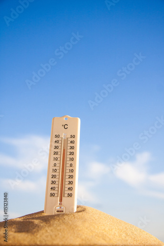 Thermometer with celsius scale on warm beach sand showing high temperature.