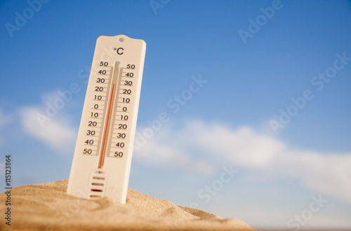 Thermometer with celsius scale on warm beach sand showing high temperature. photo