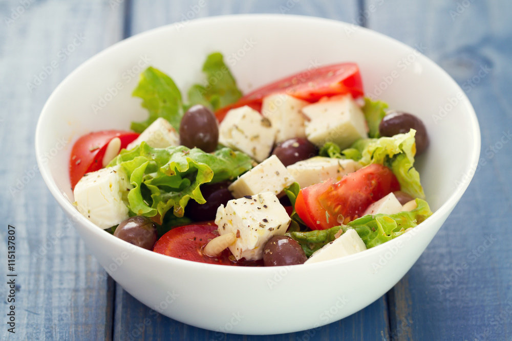 salad cheese with vegetables in white dish on blue background salad cheese with vegetables in white dish on blue background