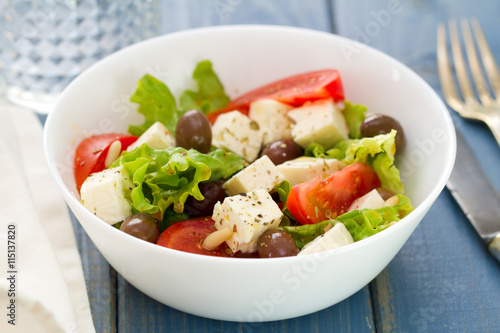 salad cheese with vegetables in white bowl on blue background